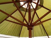 Close-up image of the umbrella's wooden ribs and pole structure holding the green fabric canopy.