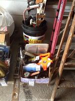 Full lot of carpenter's tools showing saws standing in bucket, levels leaning against wall, and staple gun in box