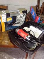 Slaymaker angle grinder in black plastic carry case next to a 141-piece tool set in a yellow-gray metal carrying case.