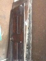 Four wooden panel doors stacked against a wall, showing varying widths and wear including chipped paint and damaged edges.