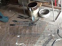 Photo showing large stoneware crock, porcelain planter bowl, metal tomato cages, and garden tools including trowel and trimming shears