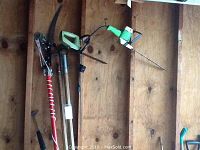 Photo showing Craftsman electric hedge trimmer, Disston cordless hedge trimmer, and various manual tree branch pruners hanging on a wooden pegboard.