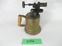 Front view of a vintage brass handheld blow torch showing the wooden handle and plunger on top.