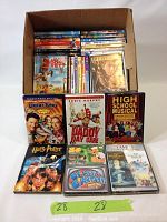 Photo of DVDs stacked inside a cardboard box and some DVDs arranged in front showing titles including Looney Tunes, Daddy Day Care, High School Musical, Harry Potter, Twilight Trilogy, and others.