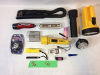 Top-down photo showing all 13 assorted flashlights and lights in varied sizes, shapes, and colors laid out on a white surface including flexible neck, handheld, pen, and keychain styles.