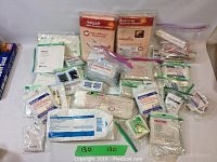 Photo showing a large quantity of assorted medical items including wound dressings, gauze pads, bandages, and applicators arranged on a flat surface.