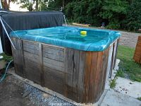 Side view of hot tub showing wood skirting and teal interior
