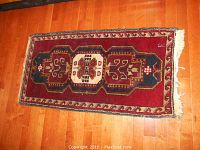 Photo of entire woven rug with fringe laid flat on wooden floor, showing pattern and wear on right side fringe.