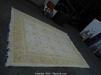 Full view of large cream area rug with yellow pattern laid flat on ground, showing overall size and fringe edges.