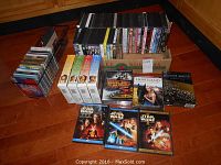 Box and racks containing approximately 50 DVDs including boxed sets and single titles plus CDs in a metal holder.