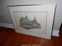 Framed black and white print of the Prince George Hotel resting against a wall and hardwood floor.