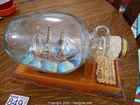 Full view of the ship in a bottle on the wooden base with the decorative stopper and plaque visible.