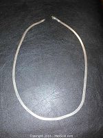 Full view of 18 inch silver herringbone chain necklace laid flat on black textured surface.