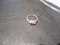 Ring lying flat on a dark surface showing the light blue center stone and side stones with silver band.