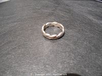 Top down view of men's silver twisted band ring on black background.