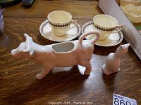 Photo showing the pair of Royal Doulton tea cups and saucers along with the ceramic cow milk pitcher and pie bird figurine on a wooden table