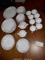 Overhead view of the entire china set including plates, cups, saucers, cream and sugar set, and serving bowls on a wood table.