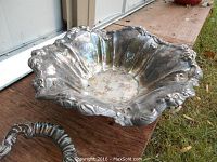 Large decorative silver plate serving bowl with floral edge, showing tarnish and wear.
