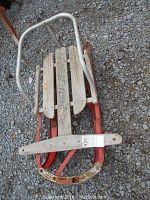 Top-down view of the vintage sleigh showing the wooden seat with three planks mounted on a red metal frame and white tubular metal handlebar.