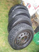 Four stacked snow tires on steel rims displayed on grass outdoors. Rims show rust and tires show tread wear.