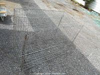 Metal folding dog kennel positioned on asphalt, showcasing the overall rectangular form and wire mesh structure.