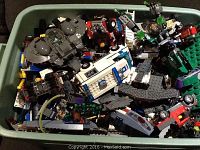 Overflow bin full of assorted Lego pieces including assembled and partly assembled kits such as a grey space shuttle-like craft, vehicles including police and fire trucks, and smaller components.