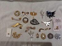 Full view of the assortment of 20 assorted costume jewelry brooches and pins on a gray fabric background.