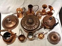 Full view of the mixed copper lot showing all items arranged on a white cloth, including kettles, pots, pitchers, and candle holders.