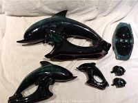 Full lot view showing three dolphin pottery figurines, two small elephant figurines with stickers, and one signed ashtray, all glazed in dark green and black tones.