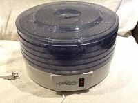 Overall view of the food dehydrator showing the five transparent trays stacked on an off-white base with power cord and a circular lid on top.