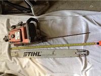 Chainsaw body with attached rusted chain bar and separate white Rollomatic bar on white cloth, tape measure laid out, wrench visible