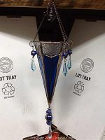 Full view of stained glass hanging tea light holder suspended by chains, showing triangular prism shape, blue and clear stained glass panels and decorative blue glass beads.