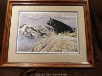 Framed lithographic print showing a black bear on rocks with snowy mountains background