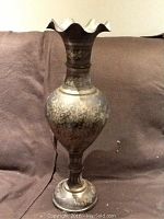 Full view of brass vase standing about 24 inches tall with scalloped top and bulbous body showing floral engraving.