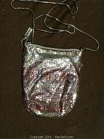 Full view of a small silver metallic purse with a shoulder strap laid flat against a dark background.