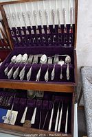 Top drawer view showing knives, forks, and spoons arranged in purple velvet slots.