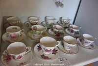 Group of twelve tea cups and saucers arranged on countertop