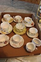 Overview of the 8 assorted tea cups and saucers with floral designs and gold trims.