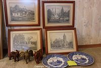 Four framed black and white prints of St Thomas landmarks, three wooden elephant figurines, and two blue and white decorative plates on the floor