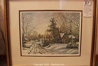 Framed print showing a snow-covered country road with trees and small wooden buildings.
