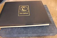 Black hardcover art book with gold logo of Peter Robson on cover lying on blue case.