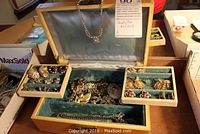Open mid century jewelry box showing blue velvet interior with multiple pieces of jewelry including necklace, earrings, brooches.