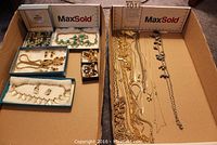 Full lot of costume jewelry items including necklaces and earring sets arranged in two cardboard boxes on carpeted floor.