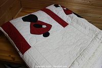 Folded hand quilted appliqued quilt with red, black, and white design showing some appliqued figures and quilting stitches.