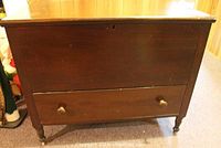 Front view of the solid wood chest showing lower drawer and turned legs with casters.
