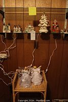Christmas village houses, ceramic tree, Santa, and small figurines on glass shelves above wicker rack holding two angel figurines in white gowns.