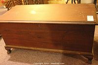 Full view of the closed cedar chest showing the dark stained wooden exterior, rectangular shape, and carved bracket feet.
