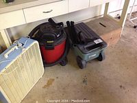 All four items together on garage floor, showing fan, shop vac, garden cart, and step stool.
