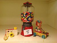 Vintage metal gum ball machine, Fisher Price toy camera, and pull toy bear in band uniform seen together on shelf.