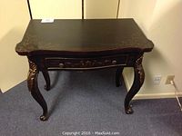 Dark painted wooden entry table with decorative floral accents and cabriole legs in a room corner.